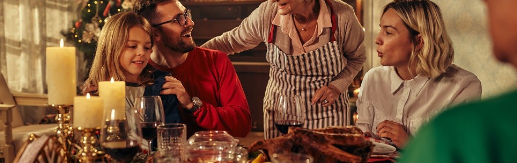 Eine Familie sitzt zusammen am Weihnachtstisch und isst. Drum herum ist es weihnachtlich geschmückt. 