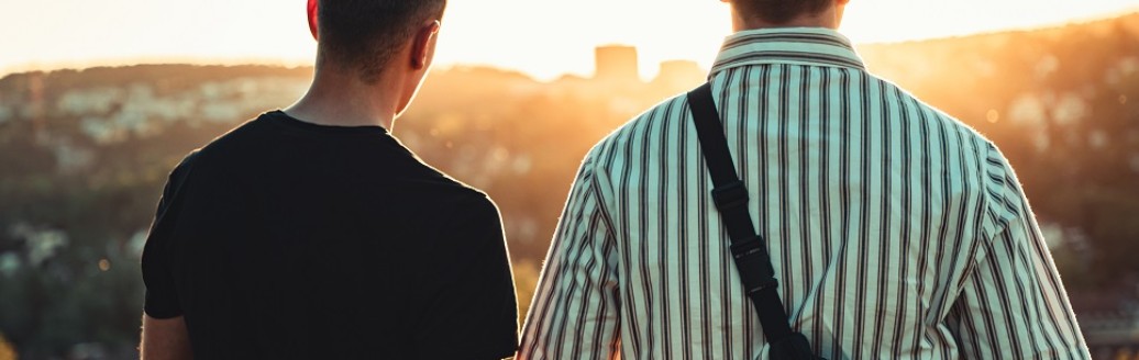 Zwei junge Männer stehen im Sonnenuntergang. Sie sind von hinten fotografiert.