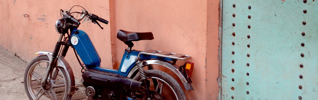 Das Bild zeigt ein älteres Moped, welches an einer Altbau-Hauswand gelehnt ist. 