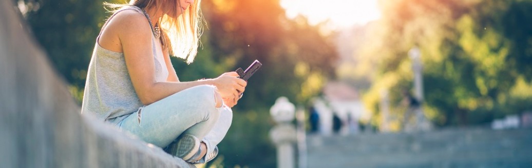 Ein Mädchen sitzt auf einer Steinmauer und schaut auf ihr Mobiltelefon. 