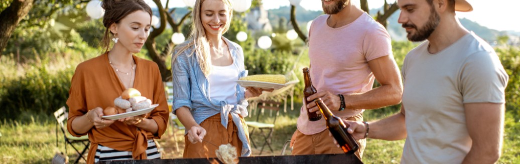 Eine Gruppe von Freunden steht zu viert an einem Holzgrill im Grünen. 