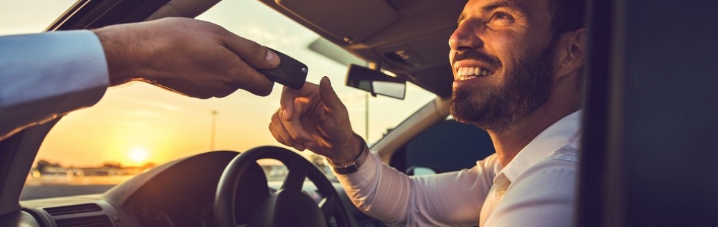 Ein Mann sitzt am Steuer eines Auto und ihm werden die Autoschlüssel gereicht. 
