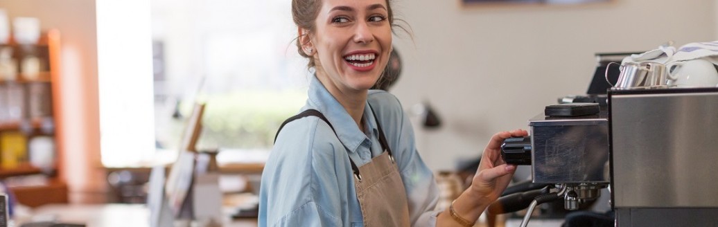 Eine junge Frau bereitet als Barista einen Kaffee an einer Kaffeemaschine in einem Café zu. 