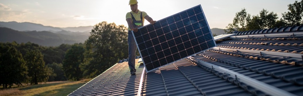 Ein Mann verlegt auf dem Dach eines Hauses Solarpanels.