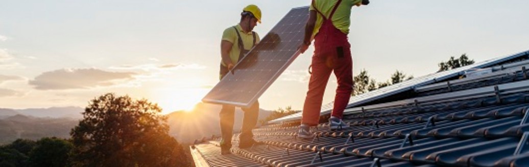 Zwei Bauarbeiter bringen eine Solaranlage auf einem Dach an.