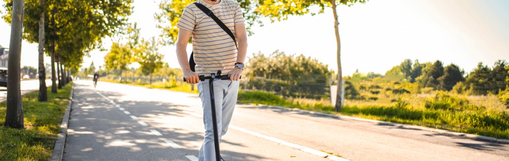 Mann trägt Schutzhelm beim Fahren mit seinem E-Scooter.