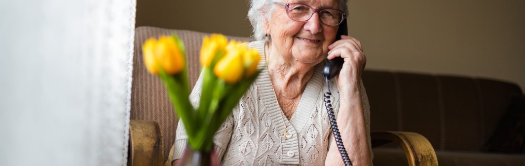 Eine ältere Dame sitzt in ihrem Zuhause am Kabeltelefon. 