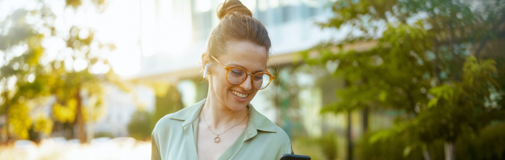 Eine junge Frau verlässt Bürogebäude und schaut glücklich auf ihr Telefon.