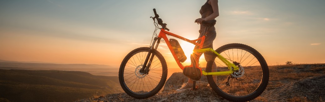 Eine Frau sitzt auf ihrem E-Bike auf einem Berg im Sonnenuntergang. 