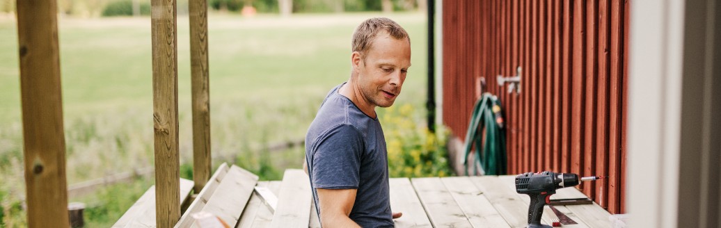 Ein Mann arbeitet an der Holzterrasse eines roten Schwedenhauses. 