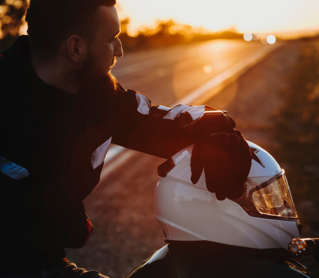 Motorradfahrer macht während einer Fahrt bei Sonnenuntergang eine Pause. Der Helm liegt auf dem Motorrad.