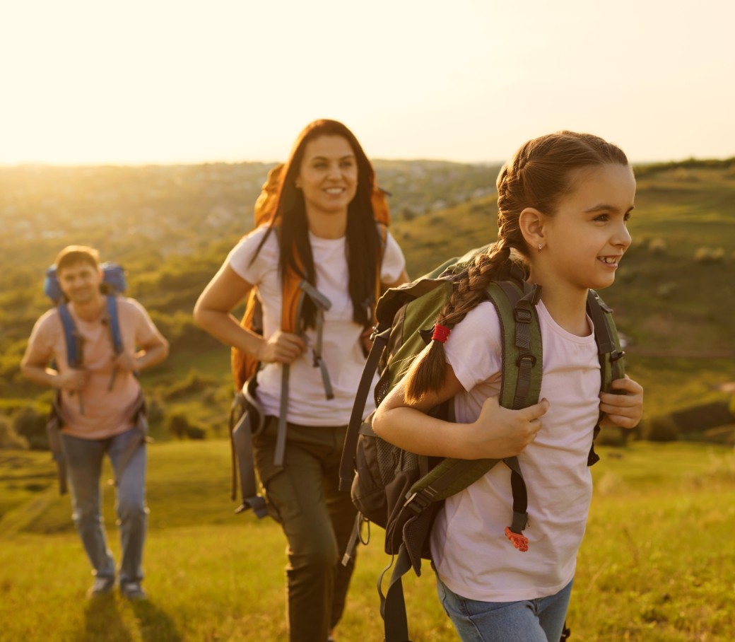 Eine junge Familie geht im Sonnenschein wandern. Die junge Tochter steht im Vordergrund.