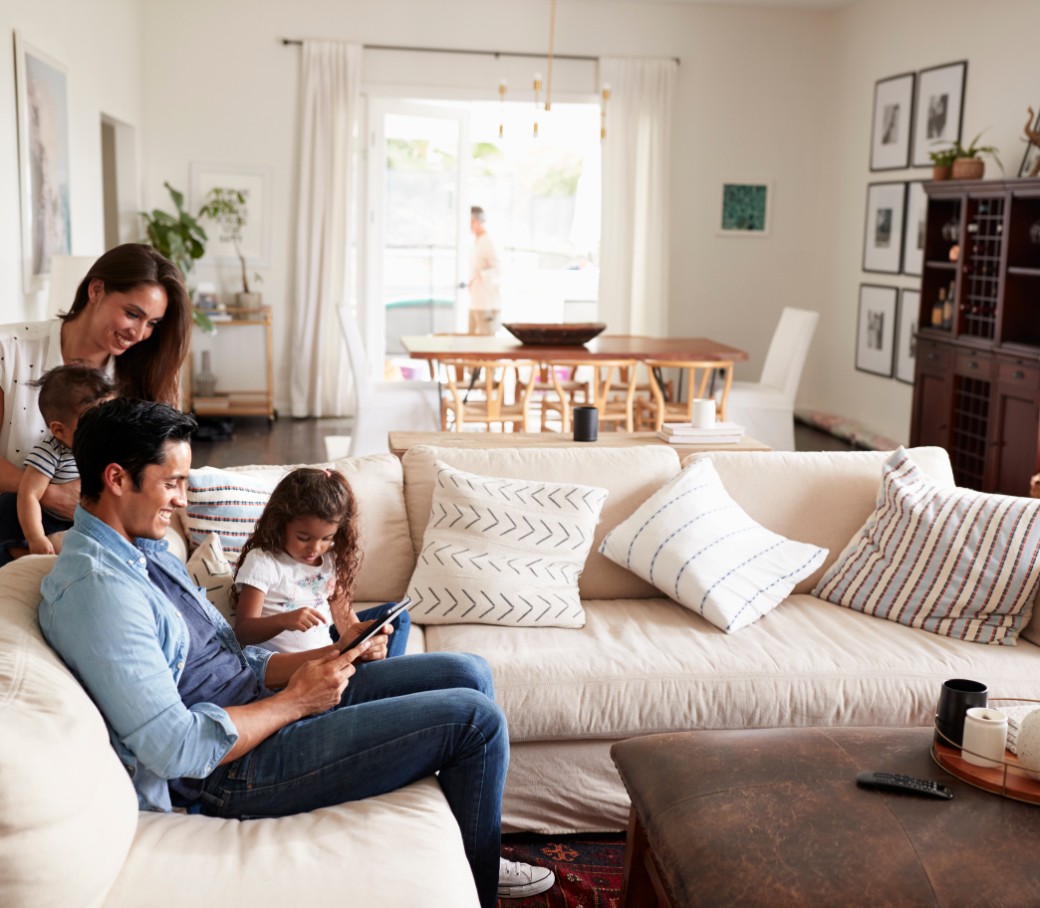 Eine vierköpfige junge Familie sitzt zusammen im Wohnzimmer auf dem Sofa. 