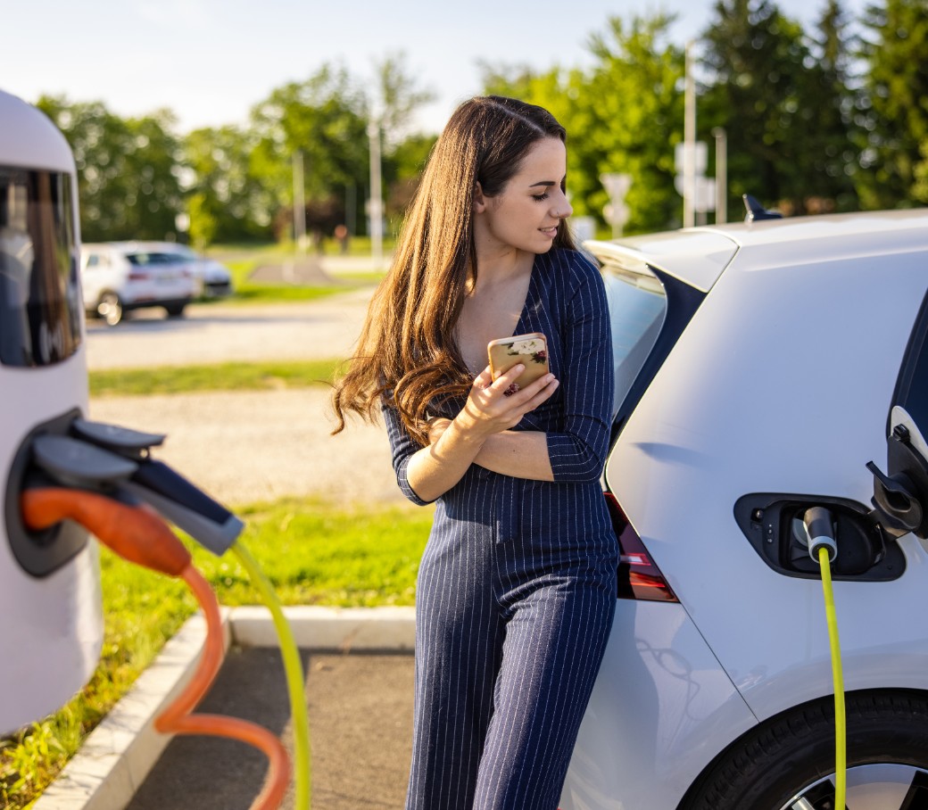 Eine junge Frau wartet bis ihr Elektroauto aufgeladen ist.