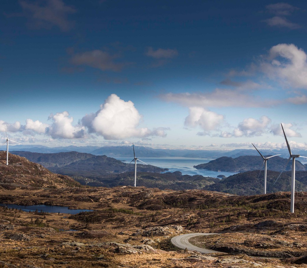Landschaft mit Windkraftanlagen auf Hügeln und Blick auf das Meer im Hintergrund.