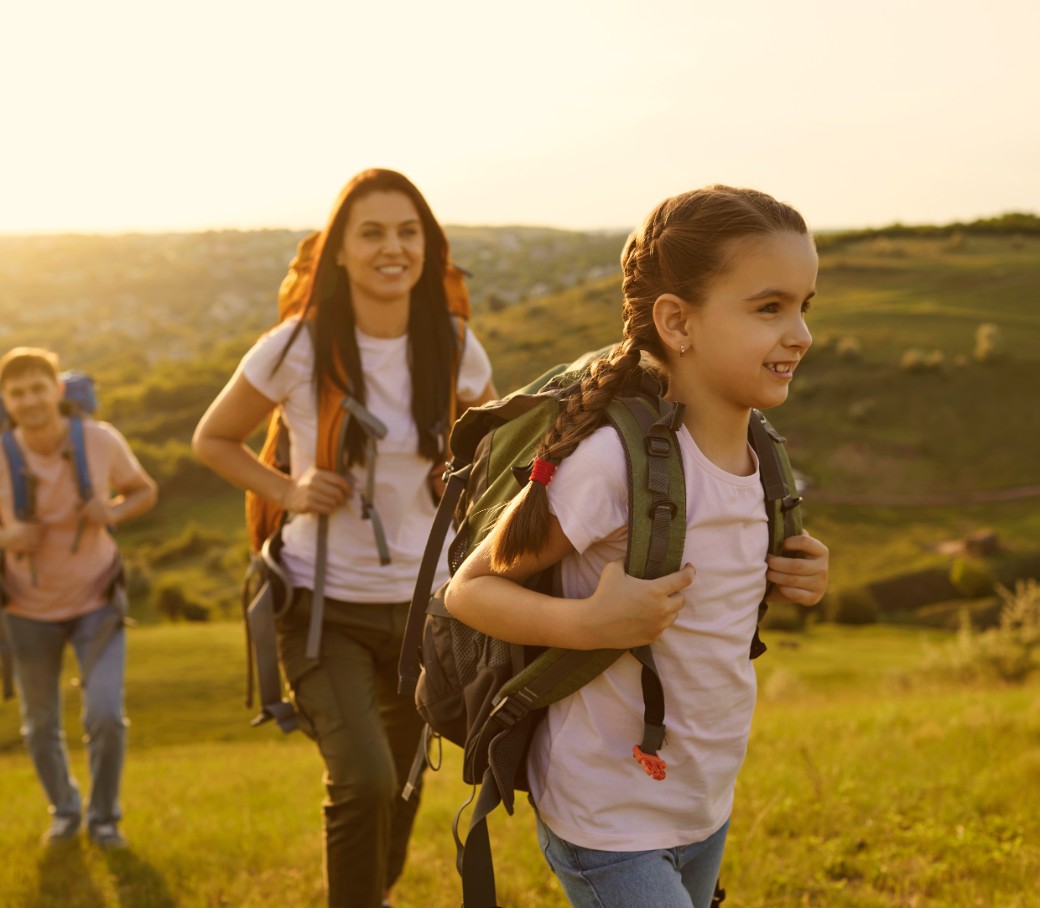 Eine junge Familie geht im Sonnenschein wandern. Die junge Tochter steht im Vordergrund.