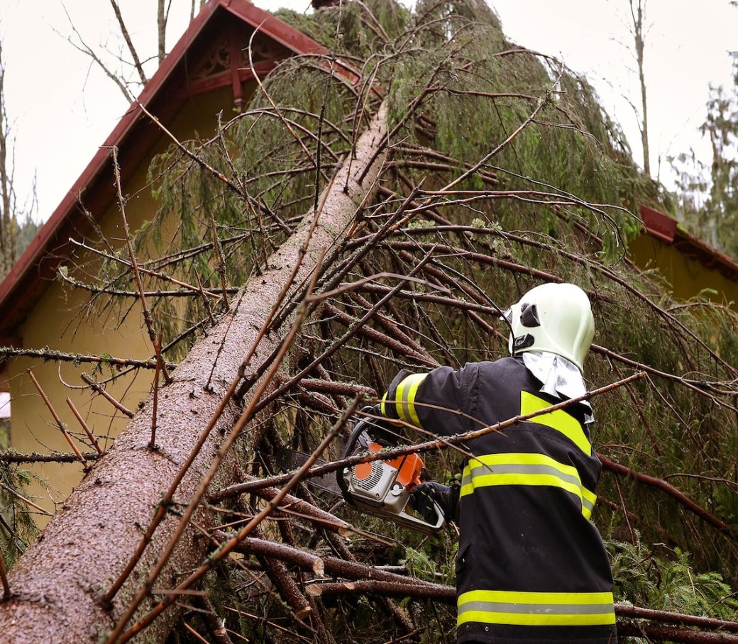 Feuerwehrmann zersägt umgestürzten Baum, der auf ein Haus gefallen ist.