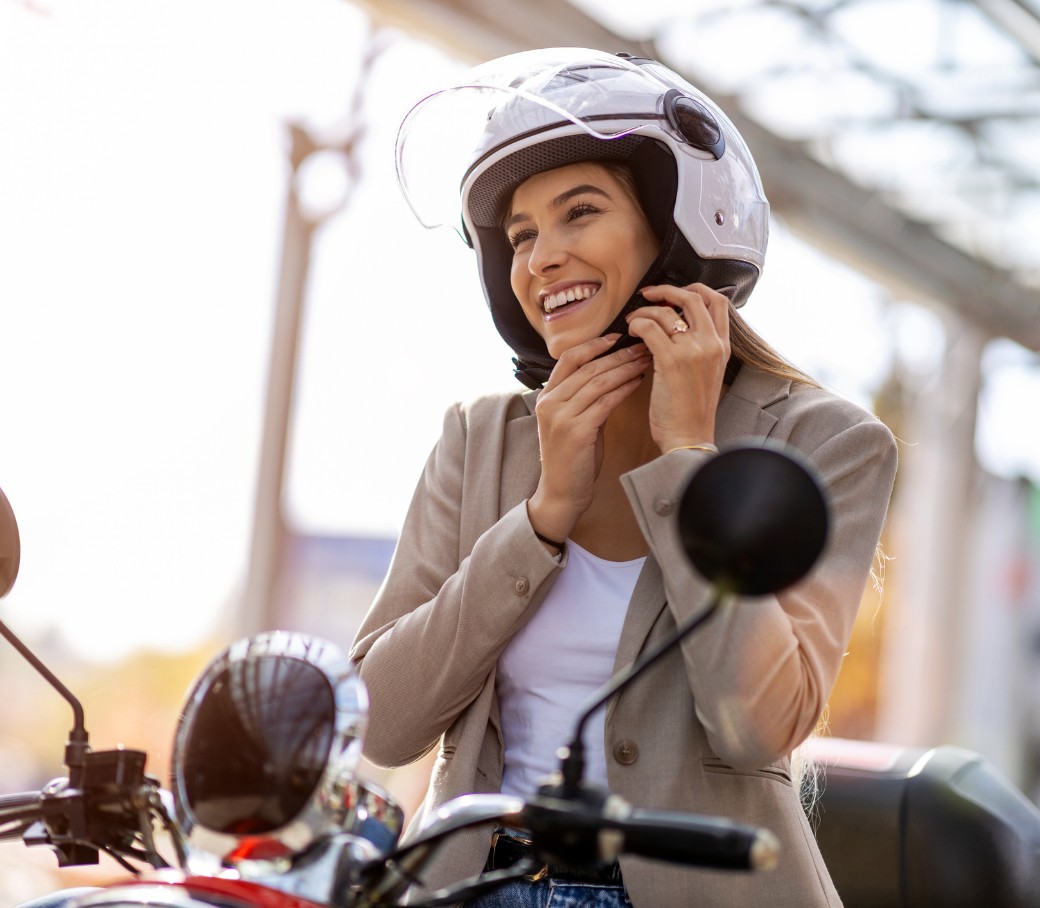 Eine junge Frau sitzt im Sonnenschein auf ihrem Moped-Roller und startet diesen.