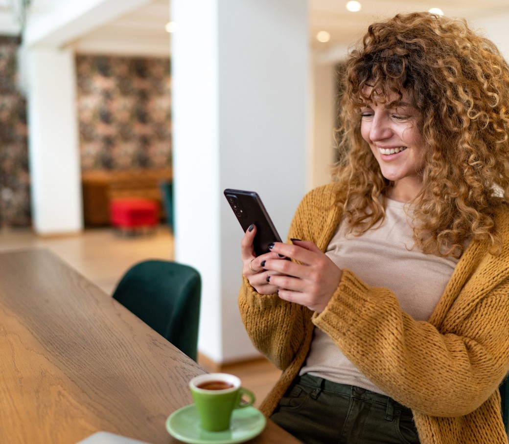 Person sitzt in einem Café und benutzt ein Smartphone, mit einer Tasse Kaffee auf dem Tisch.