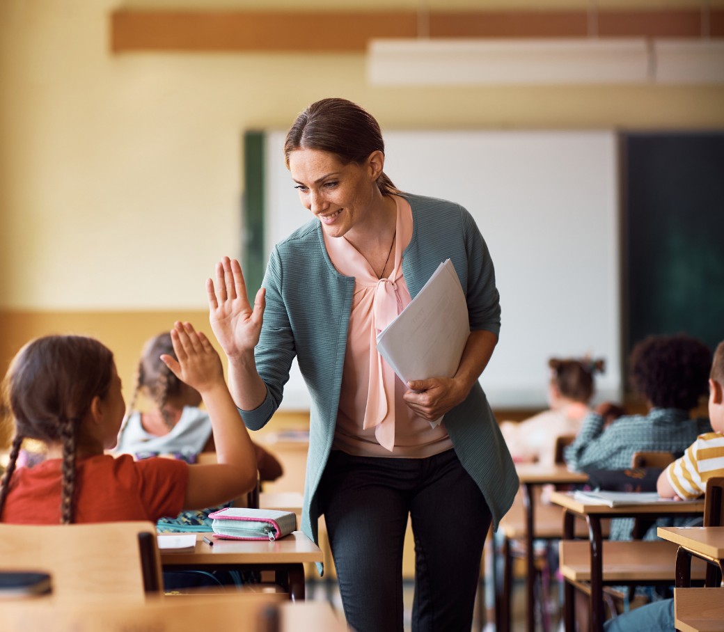 Eine Lehrerin läuft durch ihre Klasse und gibt einer Schülerin ein "high five"