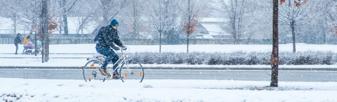 Ein Mann fährt im Schnee und durch einen leichten Schneesturm sein Fahrrad. 