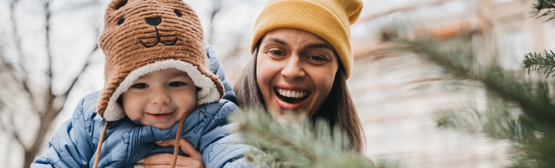 Glückliche Frau hält ihr Baby vor einem Tannenbaum.