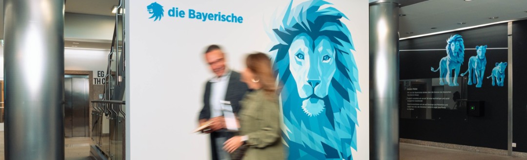 Eine Mitarbeiterin und ein Mitarbeiter der Bayerischen laufen gemeinsam durchs Foyer der Bayerischen