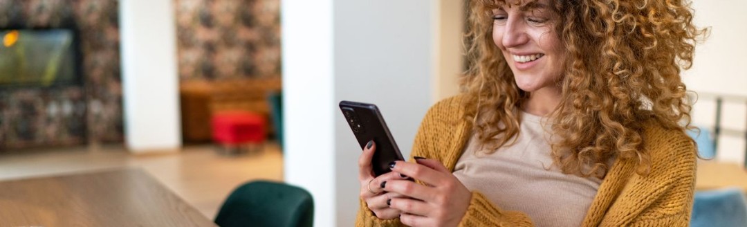 Eine junge Frau liegt auf dem Sofa und tippt lächelnd die Daten ihrer Kreditkarte in ihren Laptop ein.