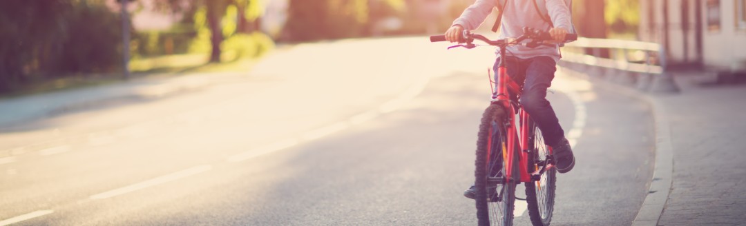 Ein junges Kind fährt mit seinem Fahrrad den Fahrradstreifen auf einer Straße entlang. 