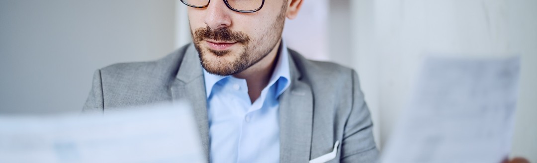 Ein Business-Mann schaut auf zwei Dokumente, die er in der Hand hält. 