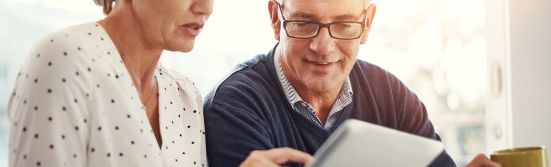 Ein Mann und eine Frau schauen gemeinsam auf ein Tablet und besprechen etwas. 