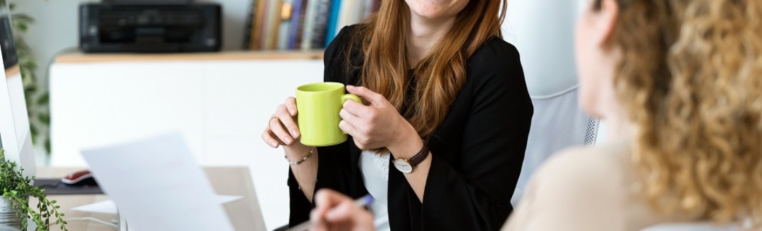 Zwei junge Frauen unterhalten sich lachend am Arbeitsplatz.