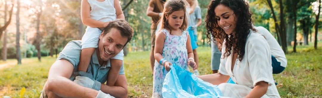 Eine junge Familie sammelt gemeinsam Müll im Grünen.