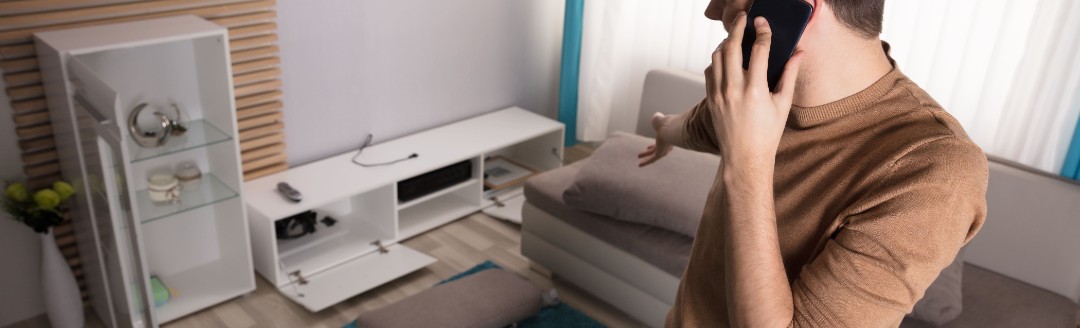 Ein junger Mann telefoniert, während er in seinem verwüsteten Wohnzimmer steht.