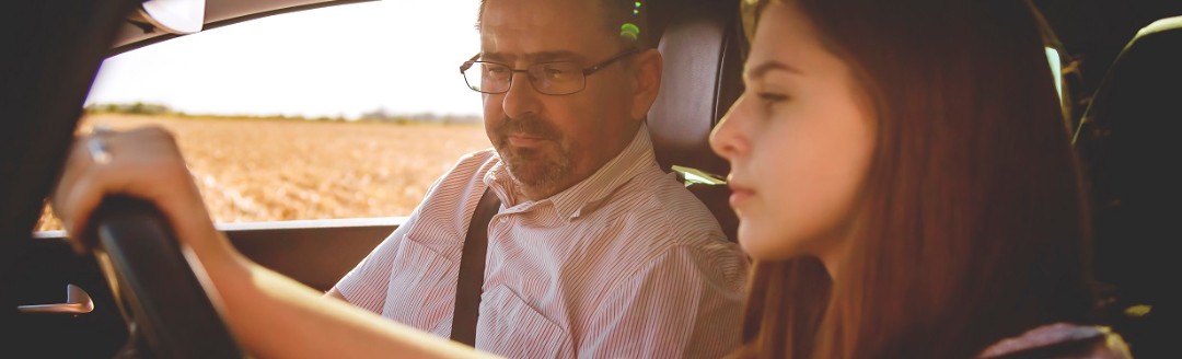 Ein junges Mädchen und ein erwachsener Mann sitzen zusammen in einem Auto. Das junge Mädchen sitzt am Steuer und lernt das Autofahren.