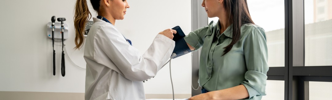 Ärztin misst einer Patientin den Blutdruck in einem Behandlungsraum.