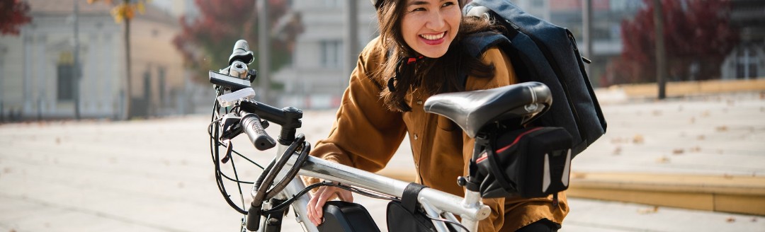 Eine junge Frau mit Rucksack und Fahrradhelm hockt vor ihrem E-Bike.