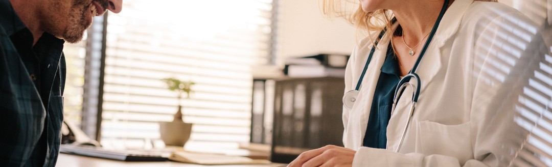 Eine Ärztin berät einen männlichen Patienten und hält ein Tablet in der Hand.