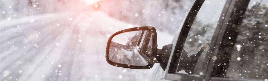 Ein weißes, seitlich fotografiertes Auto fährt durch Schnee und über eine vereiste Straße.