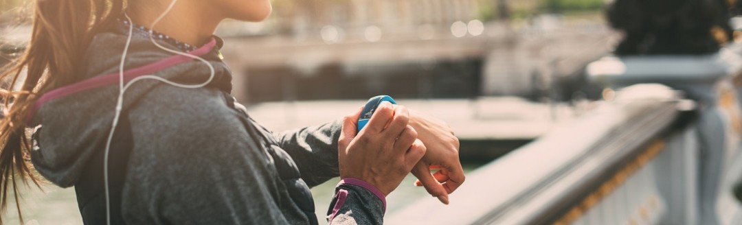 Eine junge Joggerin steht auf einer Brücke und schaut von ihrer Smart Watch hoch. 
