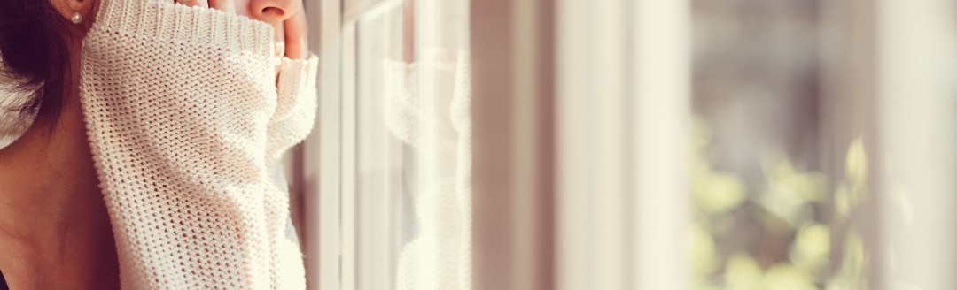 Eine junge Frau schaut aus einem Fenster in die Ferne. 