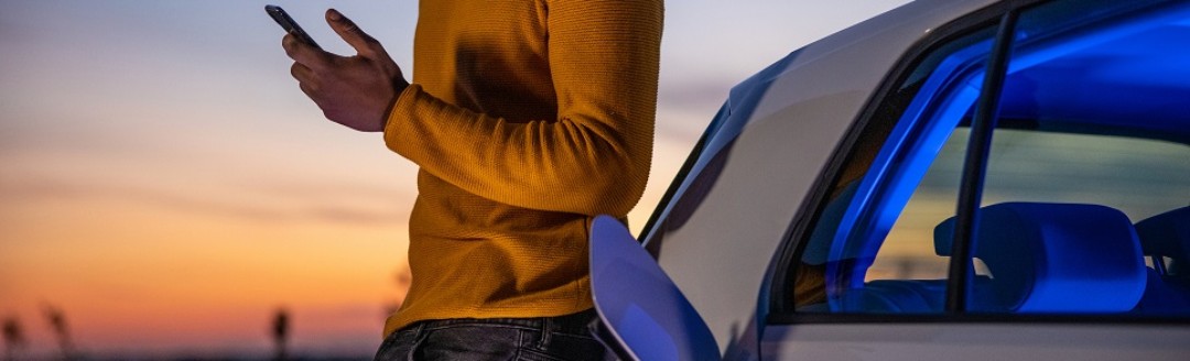 Ein junger Mann lehnt im Sonnenuntergang ein sein Elektro-Auto, während es auflädt. 