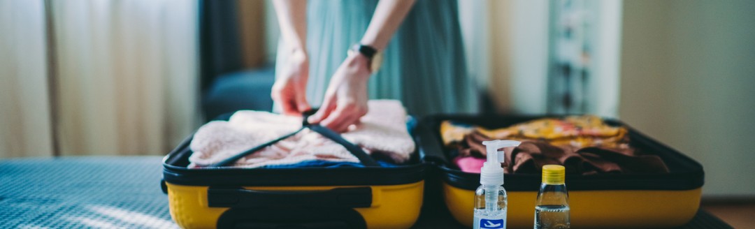 Eine Frau packt ihren Koffer auf dem Bett und hat Medikamente für die Reiseapotheke bereitgelegt. 