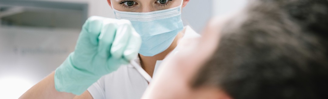 Eine Zahnärztin schaut einem Patienten in den Mund. 