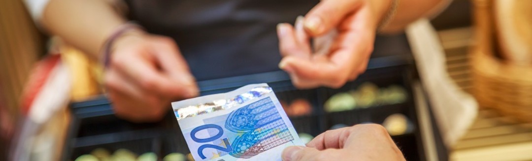 Die Hand einer Frau hält einer Kassiererin einen 20€ Geldschein hin. 