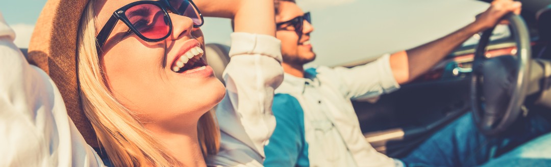 Eine Frau und  ein Mann sitzen zusammen im Cabrio und genießen das sonnige Wetter. 