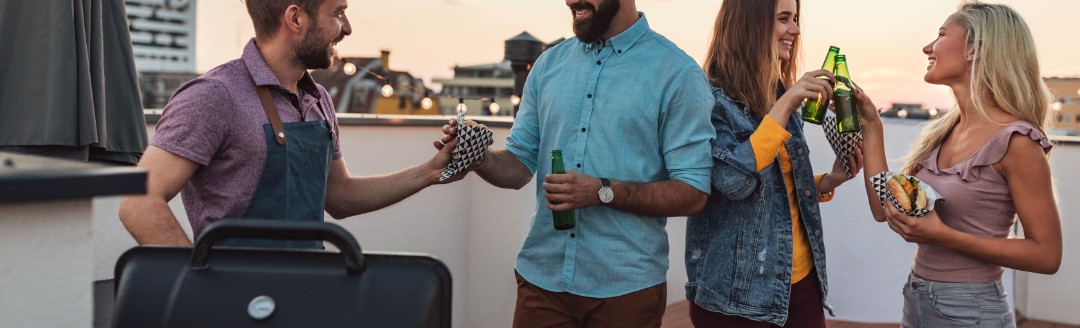 Eine Gruppe von Leuten grillt zusammen auf einer Dachterrasse. 