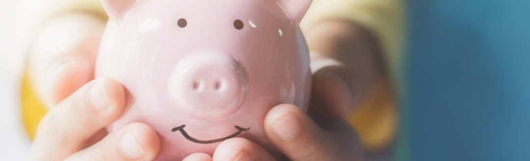 Ein kleines Kind hält ein rosafarbenes Sparschwein in die Kamera. 