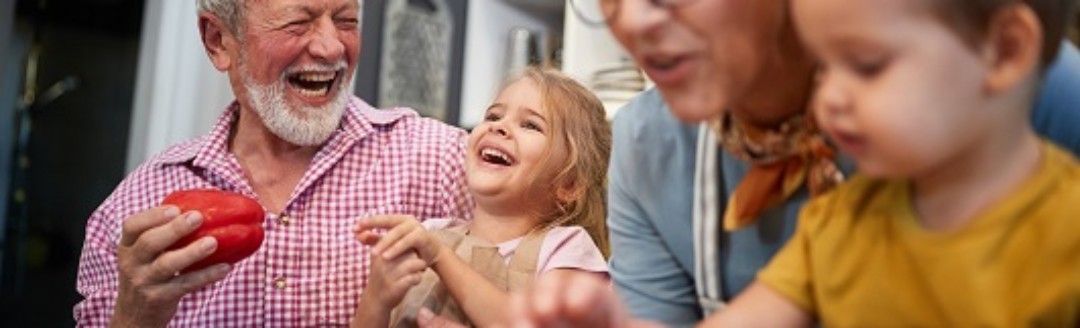 Großeltern kochen lachend gemeinsam mit ihren zwei kleinen Enkelkindern