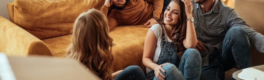 Eine Gruppe von vier Freunden sitzen zusammen zwischen Umzugskartons in einem leeren Wohnzimmer.